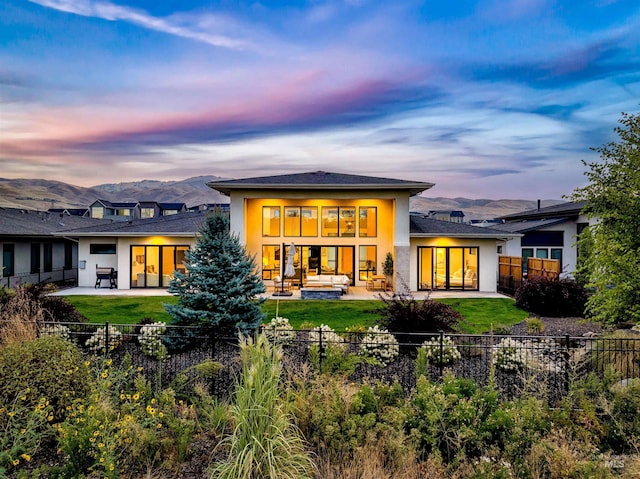 back house at dusk featuring an outdoor living space, a patio, a mountain view, and a lawn