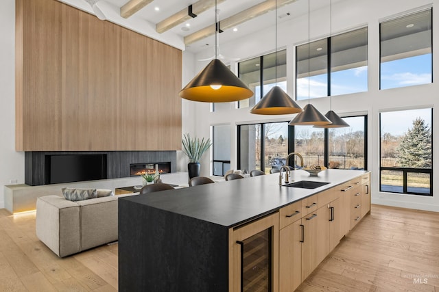 kitchen with sink, wine cooler, light hardwood / wood-style floors, a center island with sink, and light brown cabinets