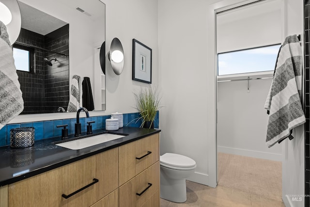 bathroom featuring tile patterned flooring, vanity, tiled shower, and toilet