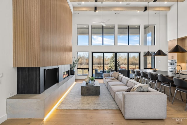 living room featuring a towering ceiling, sink, and light hardwood / wood-style flooring