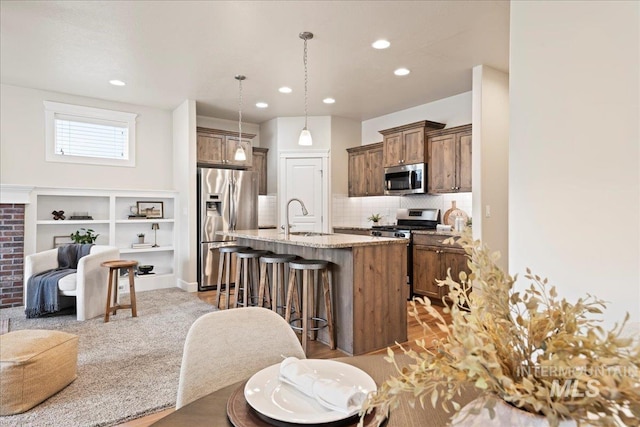 kitchen with an island with sink, appliances with stainless steel finishes, a breakfast bar, open floor plan, and light stone counters