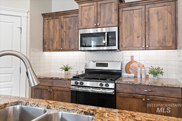 kitchen featuring a sink, appliances with stainless steel finishes, decorative backsplash, and light stone counters