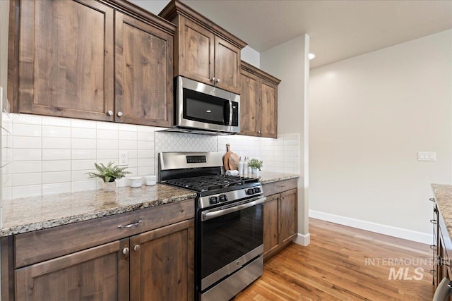 kitchen with light stone counters, baseboards, light wood-style floors, appliances with stainless steel finishes, and backsplash