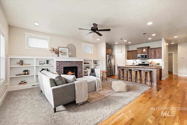 living room with a fireplace, light wood finished floors, recessed lighting, a ceiling fan, and baseboards