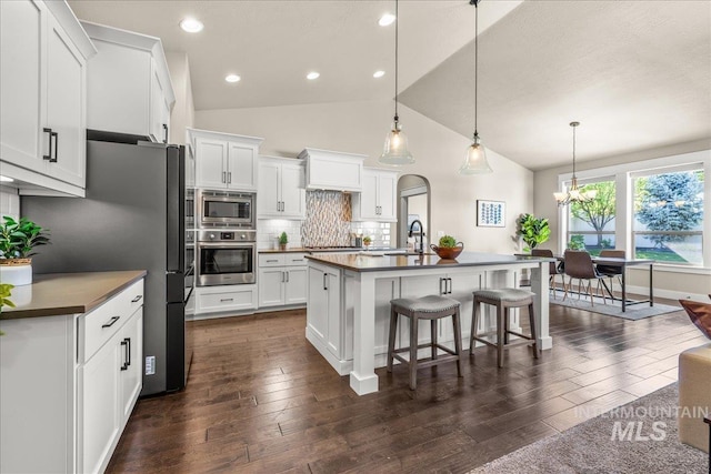 495 W Tall Prairie Dr, Meridian, ID 83642 - kitchen featuring appliances with stainless steel finishes, dark countertops, a kitchen breakfast bar, lofted ceiling, and white cabinetry