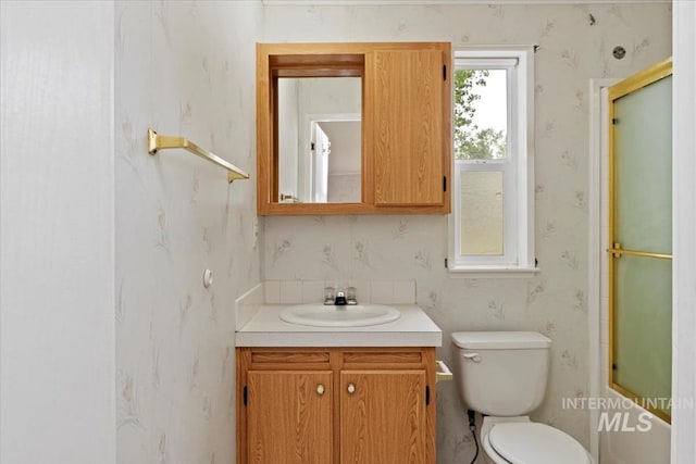 bathroom featuring toilet, a shower with shower door, vanity, and wallpapered walls