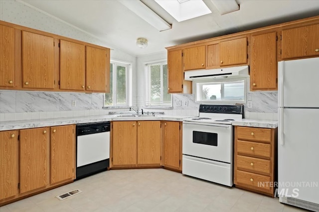 kitchen featuring white appliances, tasteful backsplash, vaulted ceiling with skylight, visible vents, and under cabinet range hood