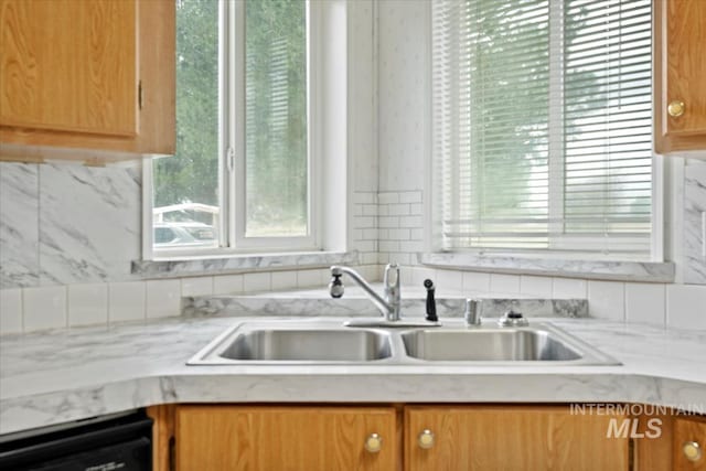 kitchen with a sink, brown cabinetry, dishwashing machine, and a healthy amount of sunlight