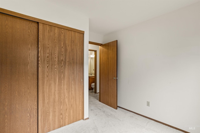 unfurnished bedroom with a closet, light carpet, and baseboards