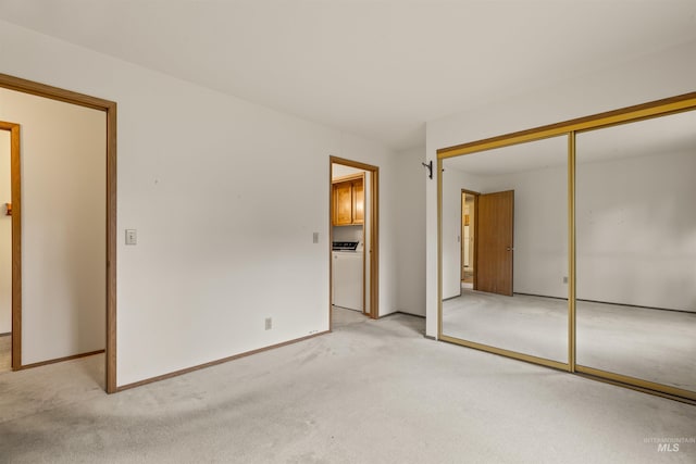 unfurnished bedroom featuring light carpet, washer / dryer, baseboards, and a closet