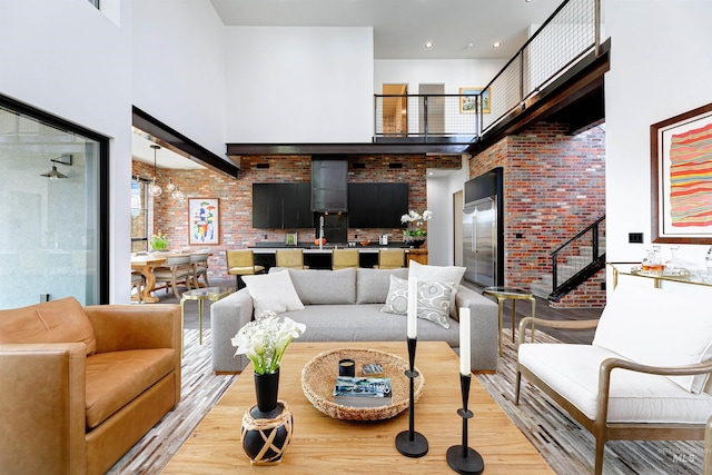 living area featuring light wood-style flooring, brick wall, and a towering ceiling