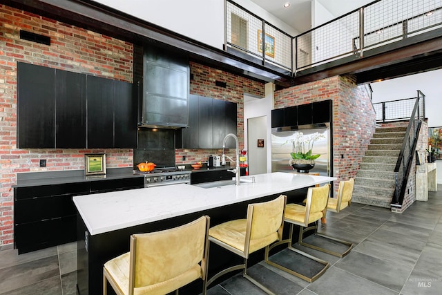 kitchen with dark cabinetry, a high ceiling, high end appliances, and a sink