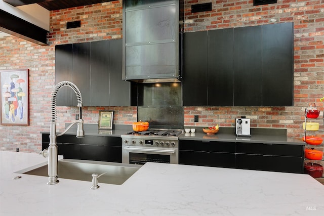 kitchen with dark cabinetry, stainless steel range, brick wall, and a sink