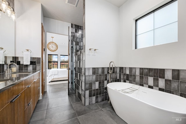 ensuite bathroom with visible vents, tile walls, a freestanding bath, ensuite bath, and a sink