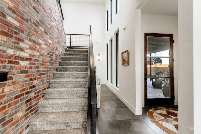 stairway featuring baseboards, a towering ceiling, and brick wall