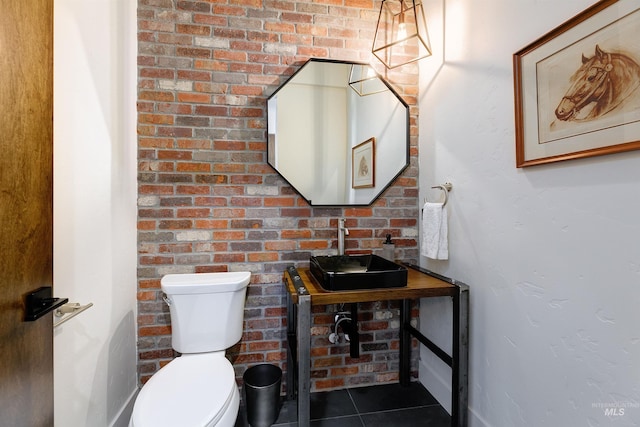 half bath with tile patterned flooring, brick wall, toilet, and a sink