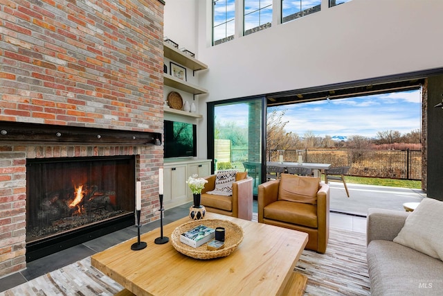 living area featuring wood finished floors, plenty of natural light, a fireplace, and a towering ceiling