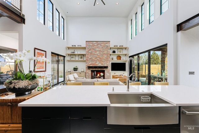 kitchen featuring a sink, open floor plan, a fireplace, light countertops, and a towering ceiling