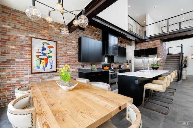 kitchen featuring brick wall, stainless steel range with gas stovetop, dark cabinetry, a towering ceiling, and a sink