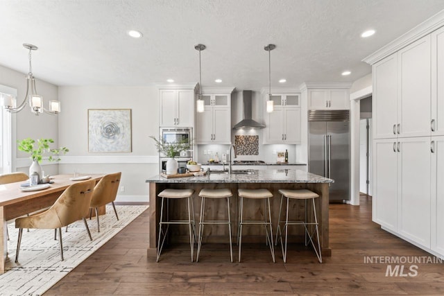 12462 S Sunrise Mist Loop, Nampa, ID 83686 - kitchen featuring built in appliances, wall chimney exhaust hood, glass insert cabinets, a breakfast bar, and white cabinetry