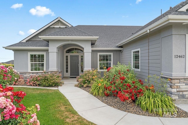 12462 S Sunrise Mist Loop, Nampa, ID 83686 - doorway to property featuring stone siding, a shingled roof, and a yard