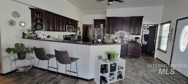 kitchen with appliances with stainless steel finishes, kitchen peninsula, a kitchen bar, ceiling fan, and dark brown cabinetry