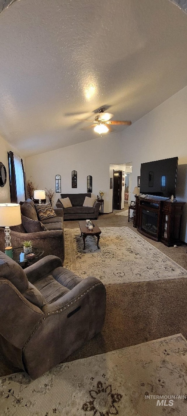 living room with vaulted ceiling, ceiling fan, carpet floors, and a textured ceiling