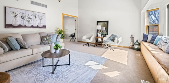 living area featuring visible vents, carpet flooring, a high ceiling, and baseboards