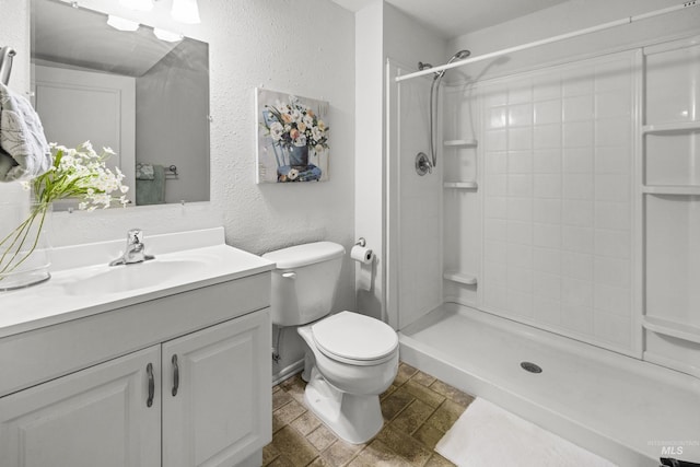 full bath featuring vanity, toilet, a textured wall, and a tile shower