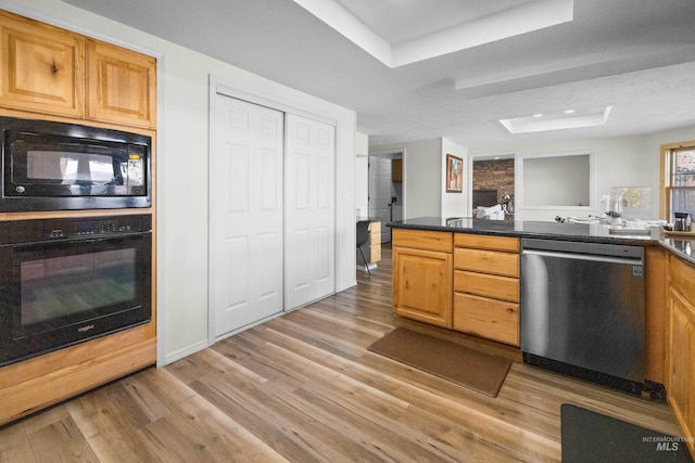 kitchen featuring dark countertops, black appliances, a tray ceiling, and light wood-style floors