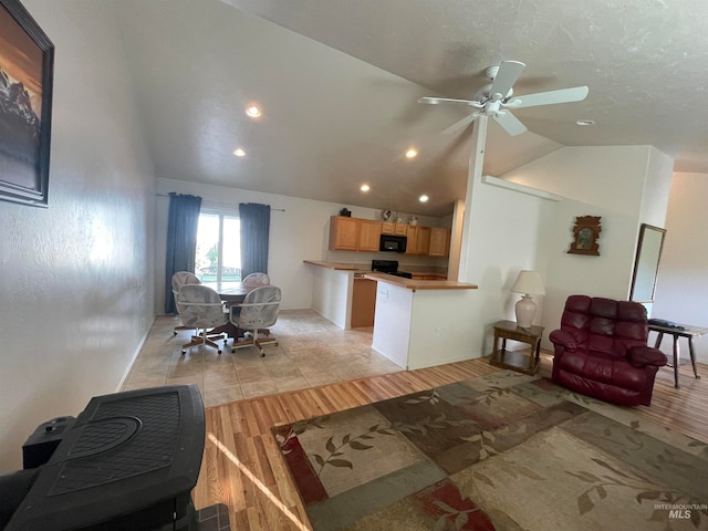 living room with ceiling fan, light hardwood / wood-style floors, and vaulted ceiling