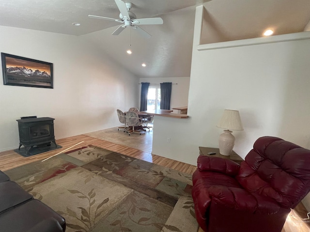 living room with light wood-type flooring, vaulted ceiling, a wood stove, and ceiling fan