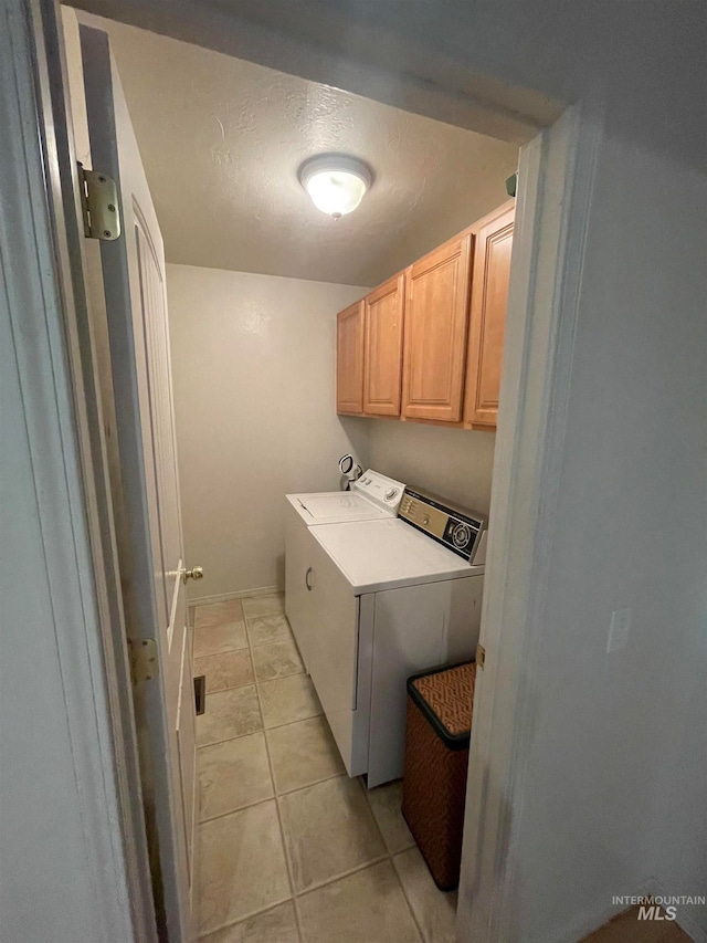 laundry room with light tile patterned flooring, a textured ceiling, cabinets, and washer and dryer