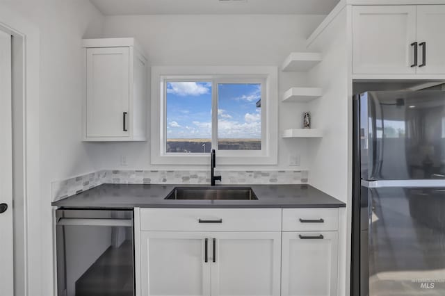 kitchen with a sink, dark countertops, stainless steel dishwasher, and freestanding refrigerator