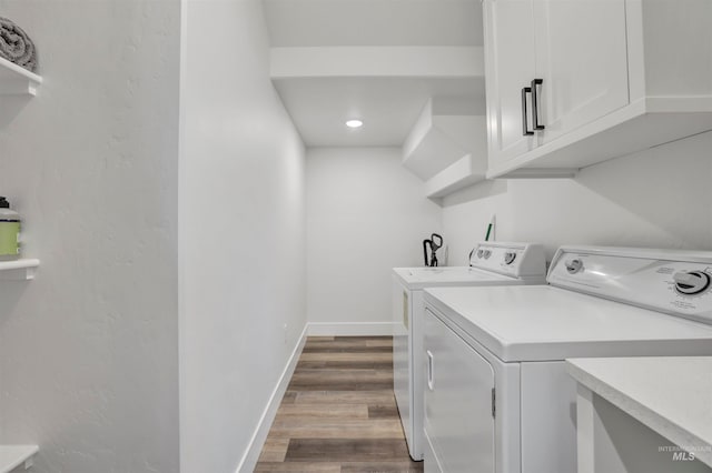 clothes washing area featuring washer and clothes dryer, wood-type flooring, and cabinets