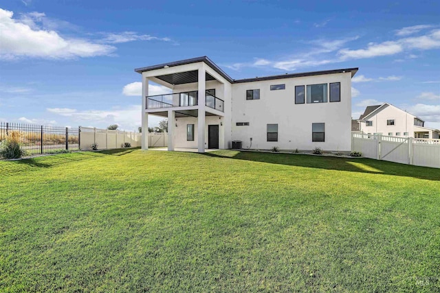 back of house featuring a fenced backyard, stucco siding, a yard, central AC, and a balcony
