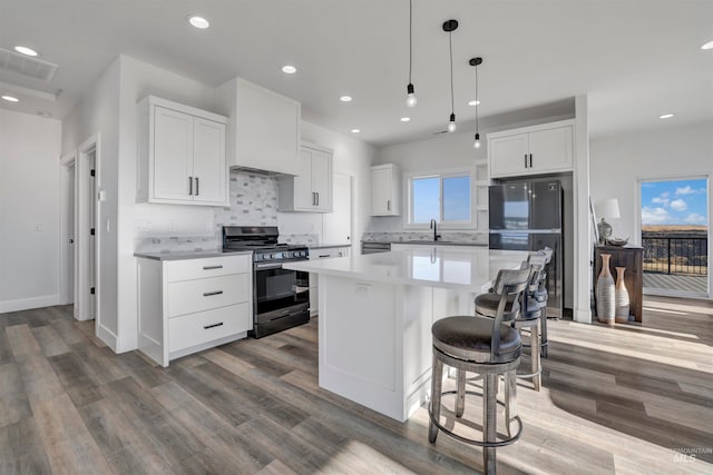 kitchen with white cabinets, pendant lighting, black gas stove, hardwood / wood-style flooring, and a center island