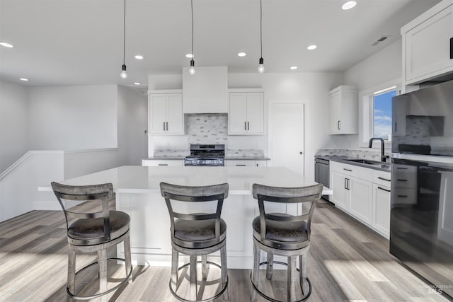kitchen with wood finished floors, decorative backsplash, stainless steel gas stove, a sink, and a center island