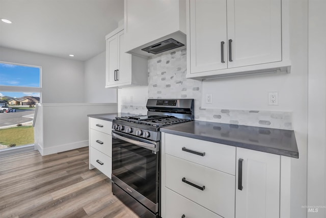 kitchen featuring light wood-type flooring, tasteful backsplash, custom range hood, stainless steel gas range, and white cabinetry