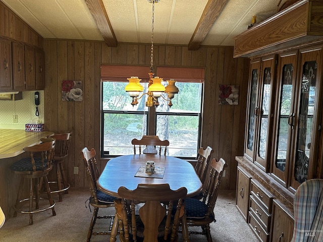 dining space featuring carpet, beamed ceiling, a healthy amount of sunlight, and an inviting chandelier