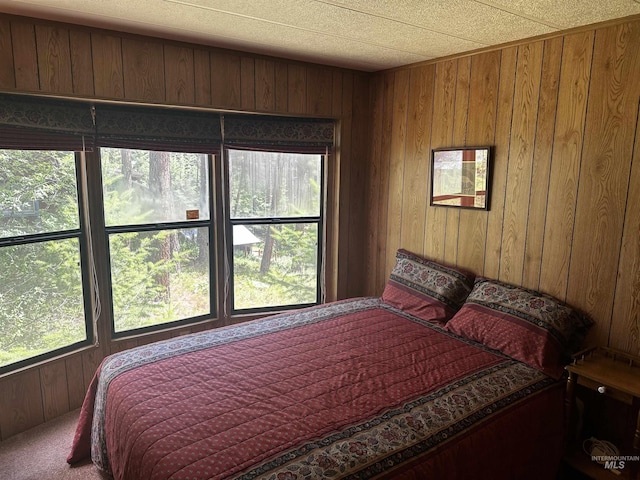 bedroom with carpet flooring, multiple windows, and wooden walls