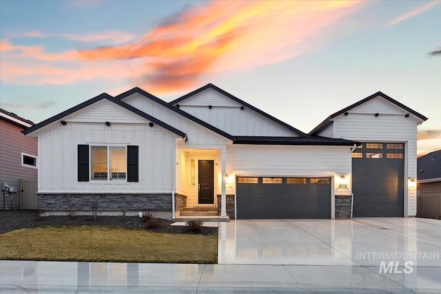 view of front facade with an attached garage, stone siding, driveway, and board and batten siding