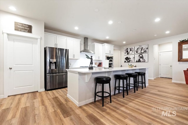 kitchen featuring a large island, wall chimney range hood, white cabinets, and appliances with stainless steel finishes