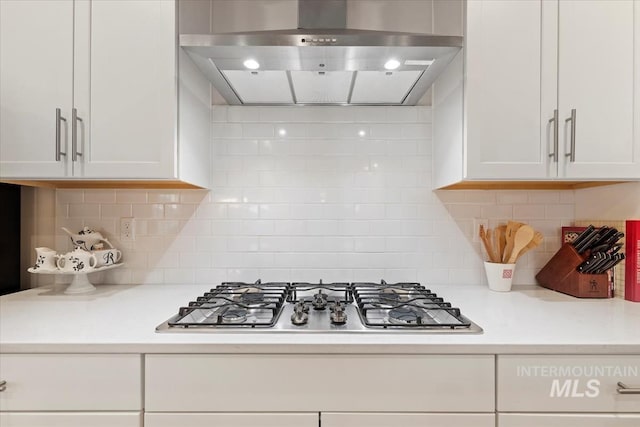 kitchen featuring decorative backsplash, stainless steel gas cooktop, white cabinets, and wall chimney exhaust hood