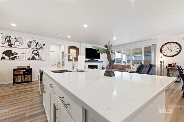 kitchen featuring sink, white cabinets, light stone countertops, a center island with sink, and light wood-type flooring