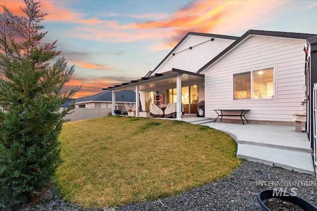 back house at dusk featuring a patio area and a lawn