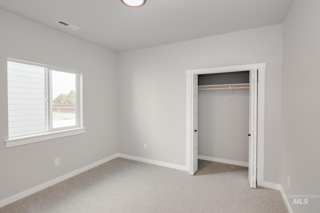 unfurnished bedroom featuring light colored carpet, baseboards, a closet, and visible vents