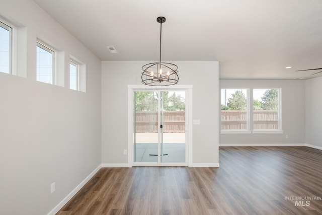 unfurnished dining area with an inviting chandelier, plenty of natural light, wood finished floors, and baseboards