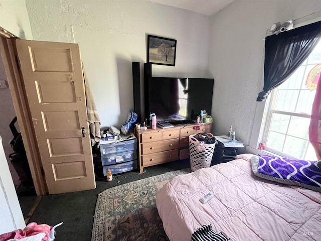 bedroom featuring dark colored carpet, a textured wall, and multiple windows
