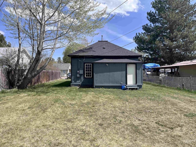 back of house with an outdoor structure, a fenced backyard, a shingled roof, and a lawn